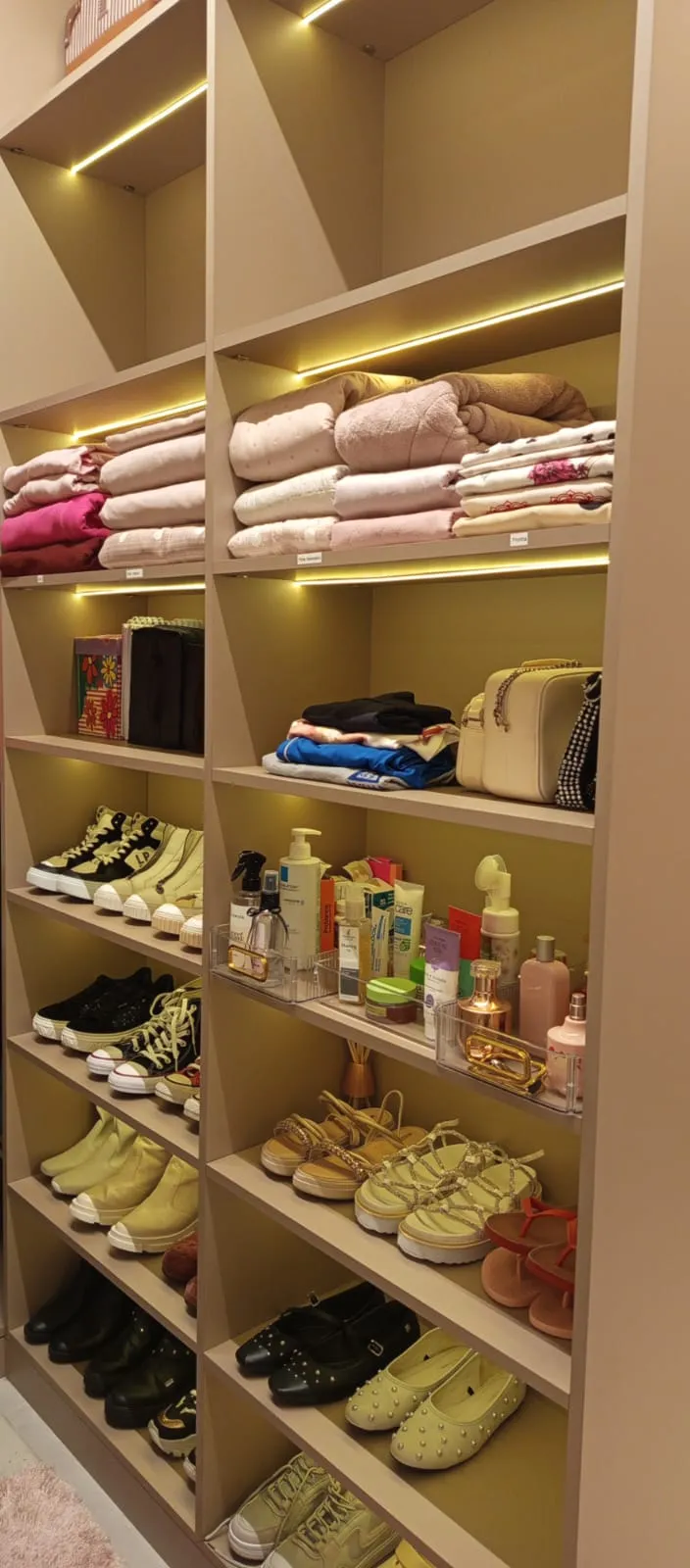 O mesmo armário com cobertores dobrados, sapatos separados por tipo e cosméticos em bandejas de acrílico