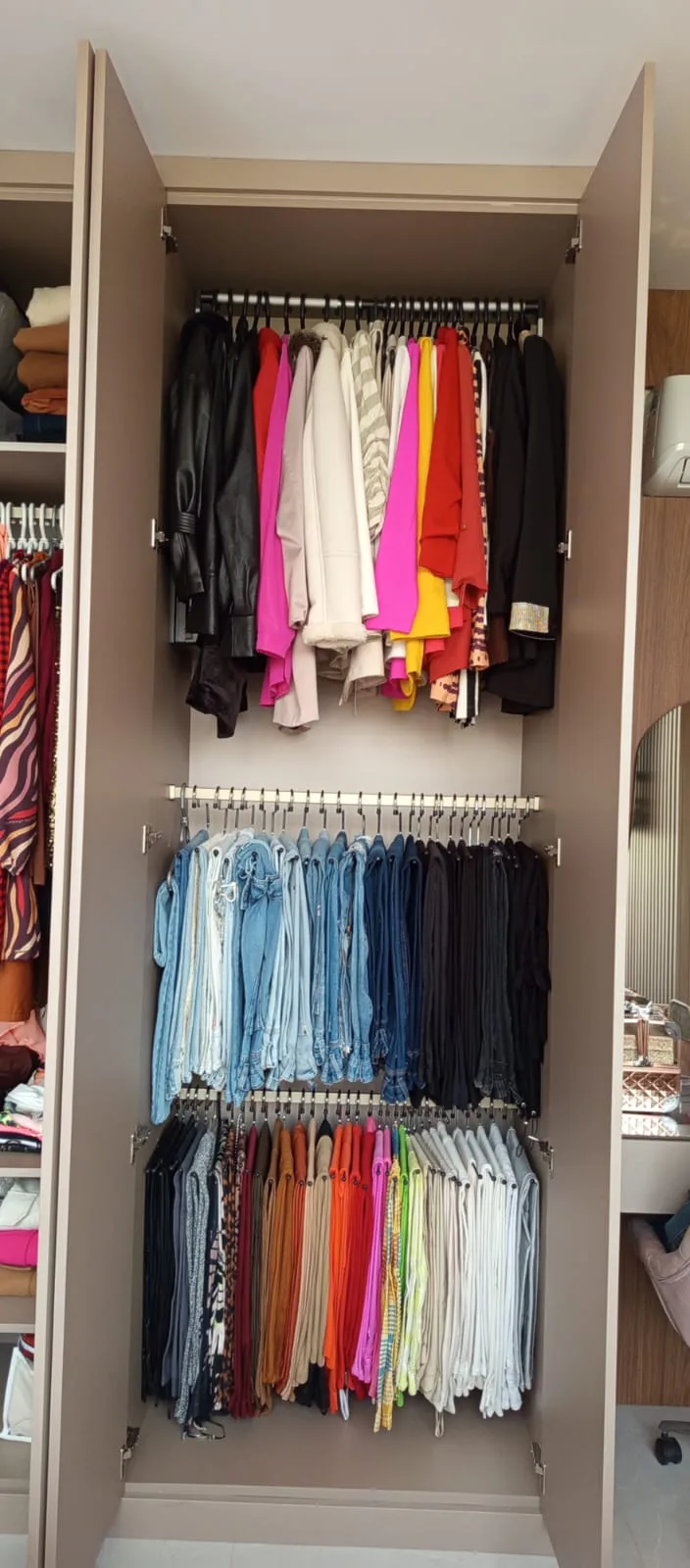 O mesmo guarda-roupa com casacos, jeans e calças em barras separadas e organizados por cor